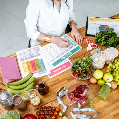 Dietitian writing a diet plan, view from above on the table with different healthy products and drawings on the topic of healthy eating